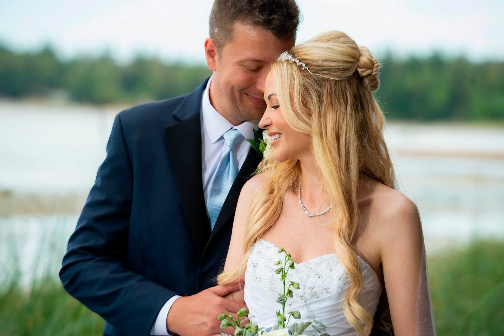 The newlyweds cheek to cheek by the water, Charlene's hair half up with a tiara