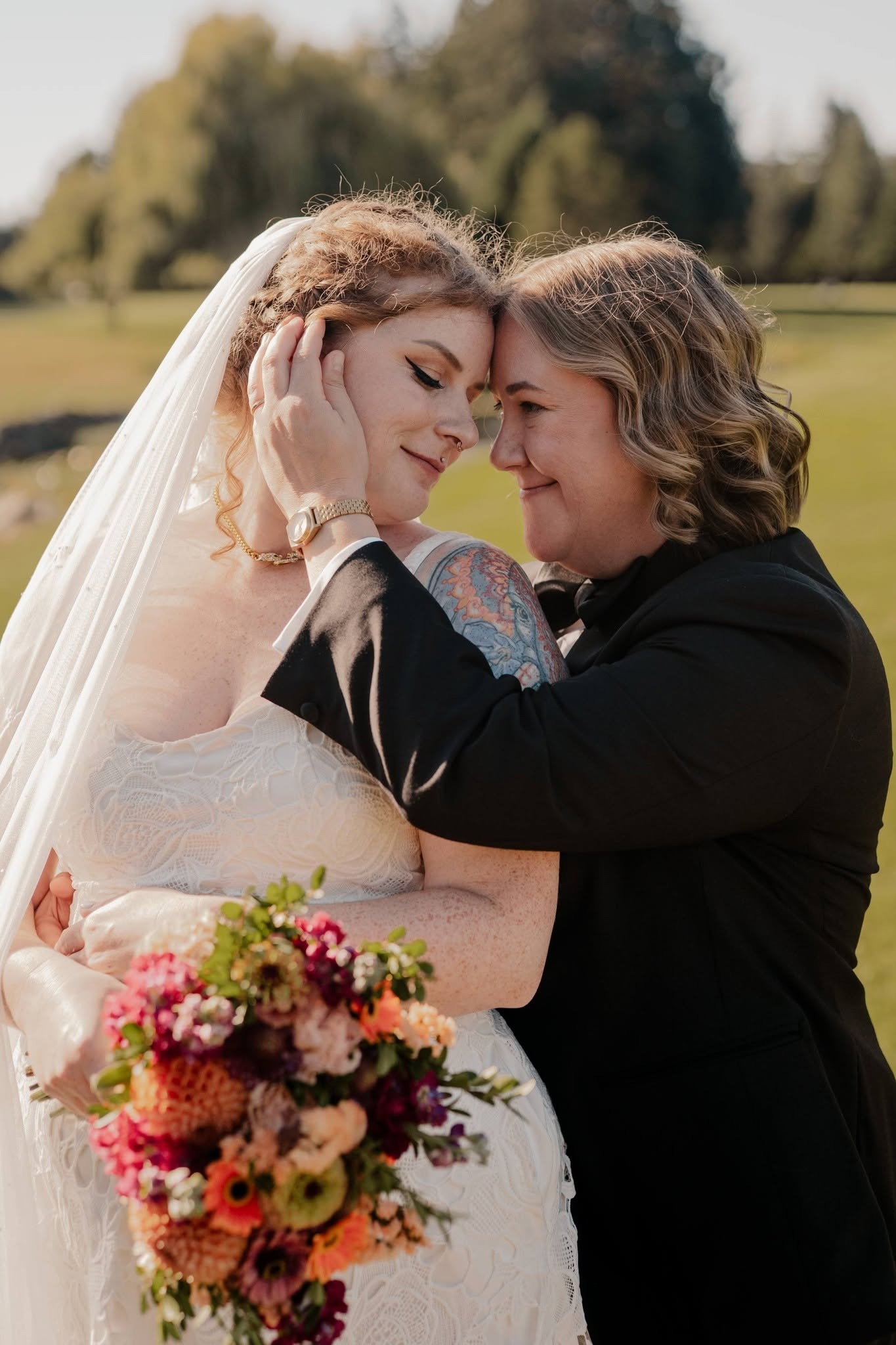 The newlyweds touching foreheads on the golf course, holding a bright bouquet