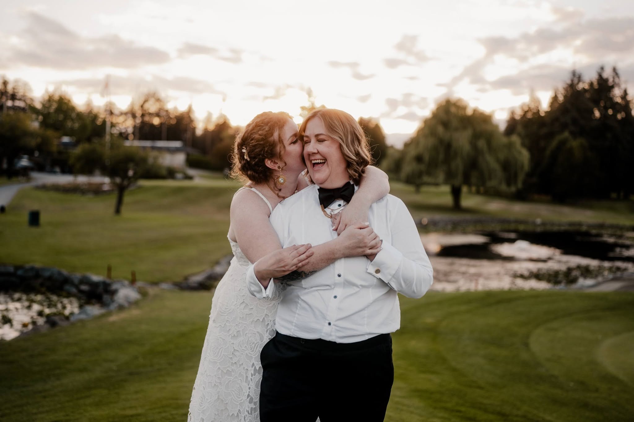 The newlyweds laughing in a hug by the pond at sunset