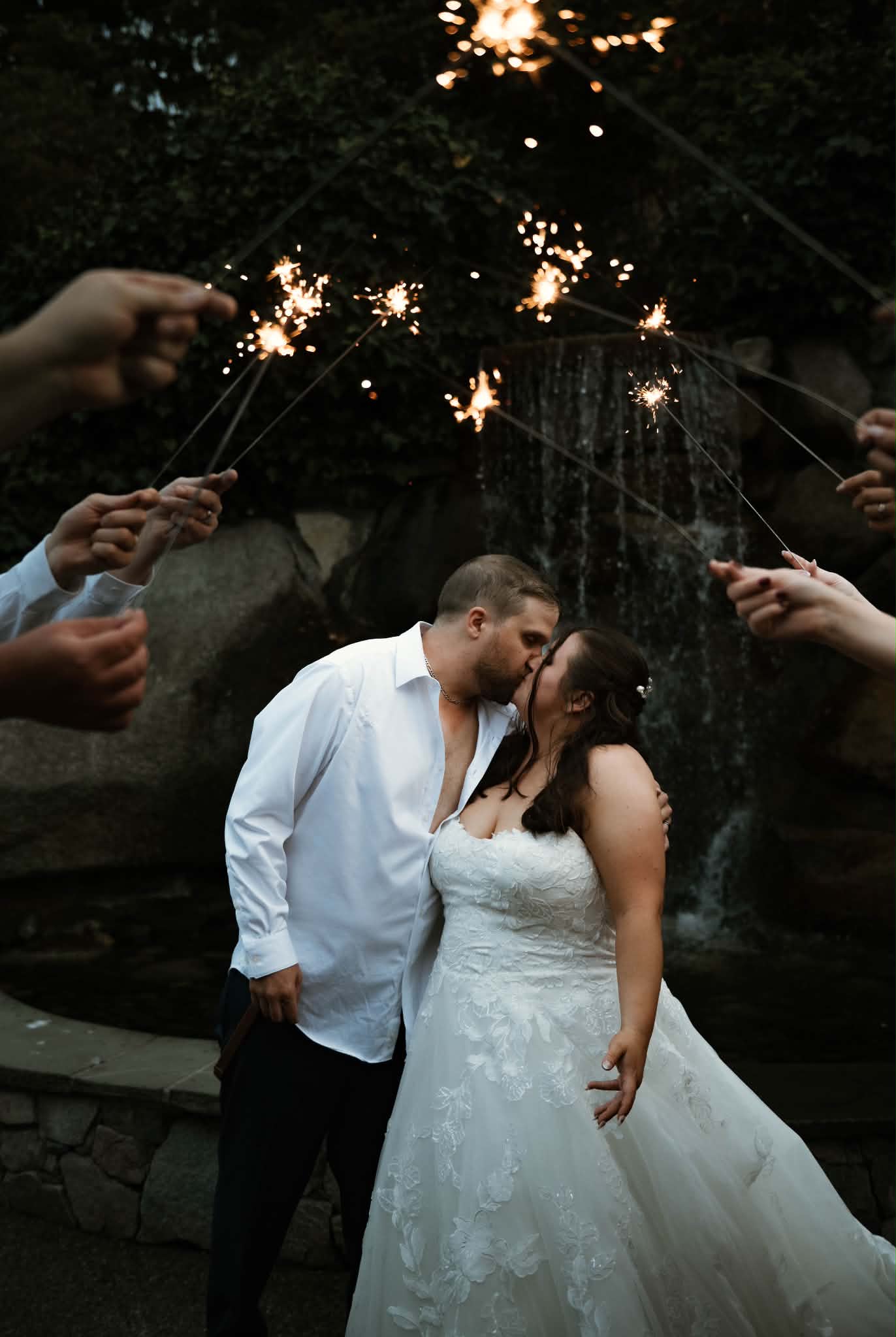 Emily and Sheldon kissing under a sparkler arch in front of the waterfall at Inn at Laurel Point