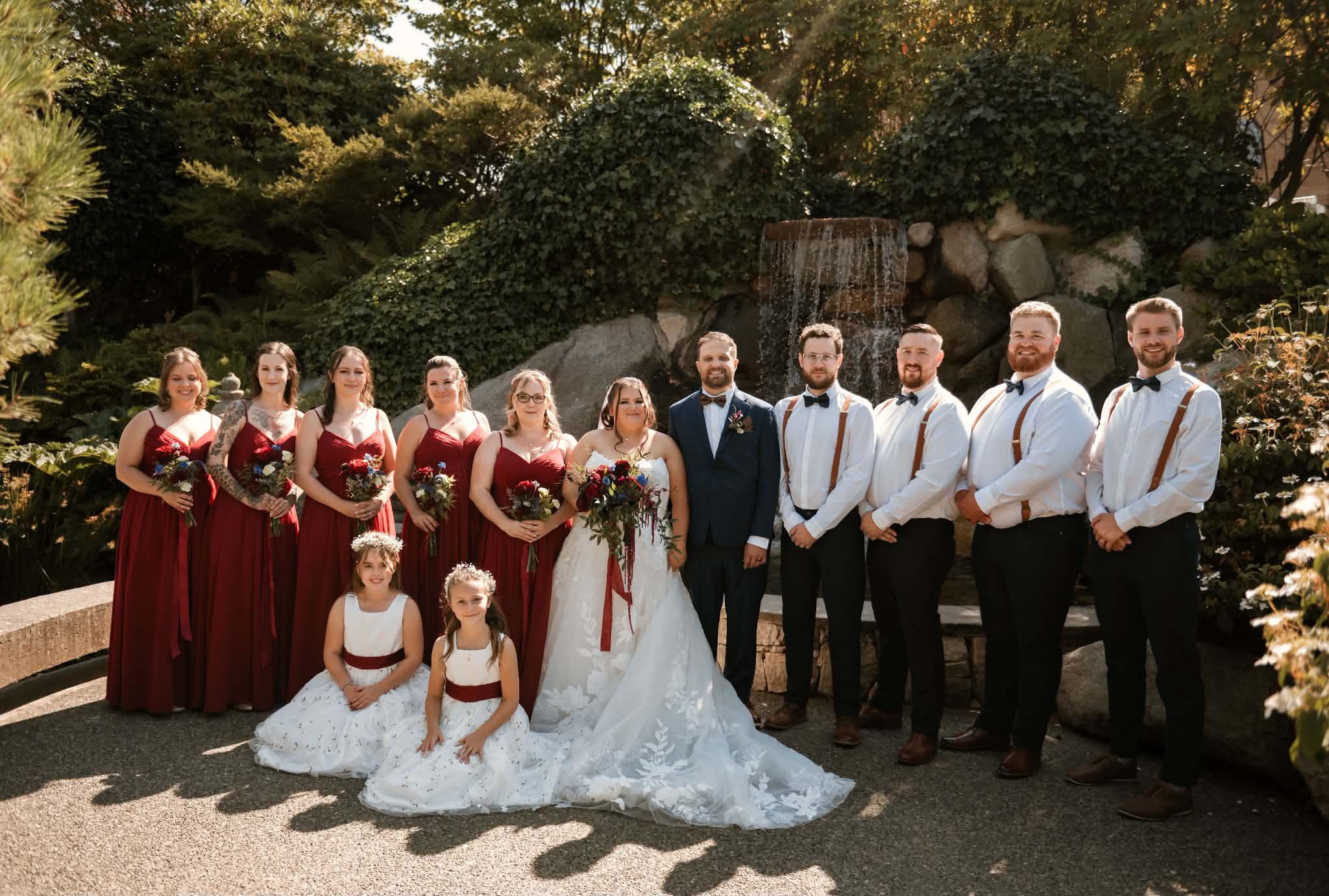 The full wedding party and two flower girls in front of the waterfall at Inn at Laurel Point